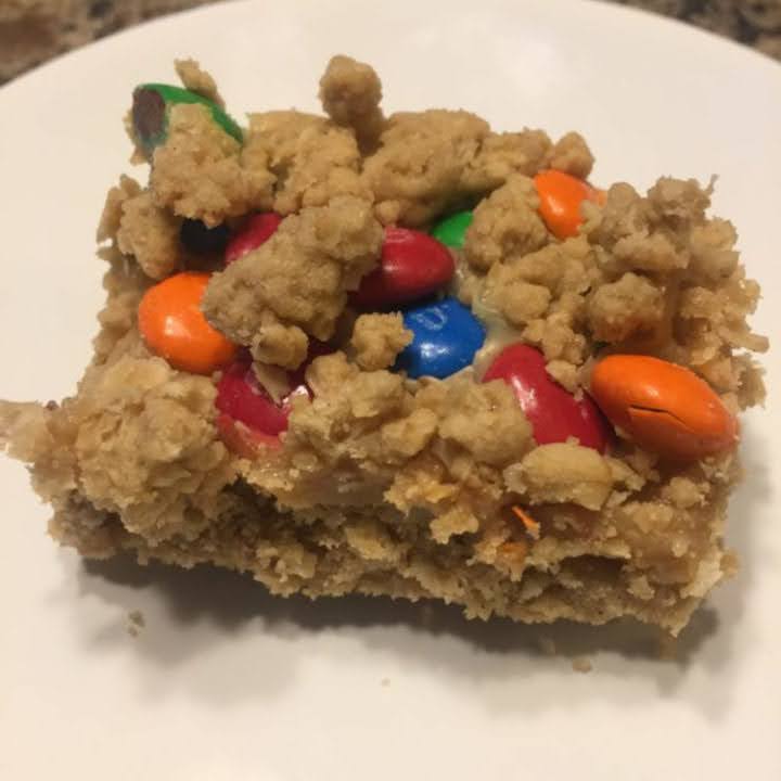 Close-up of an M&M bar with an oatmeal crust, peanut butter filling, and colorful M&M candies sprinkled on top.