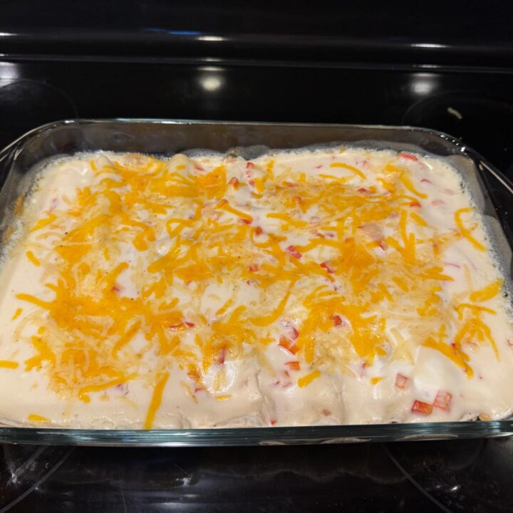 A glass baking dish filled with creamy chicken enchiladas, topped with melted cheddar cheese and diced red bell peppers.