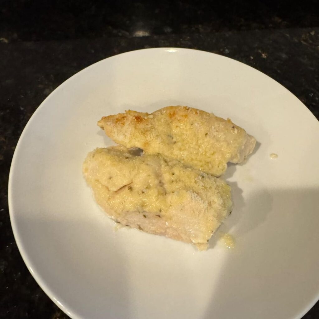 A baked chicken breast coated in a mixture of Italian seasoning and Parmesan cheese, served on a white plate.